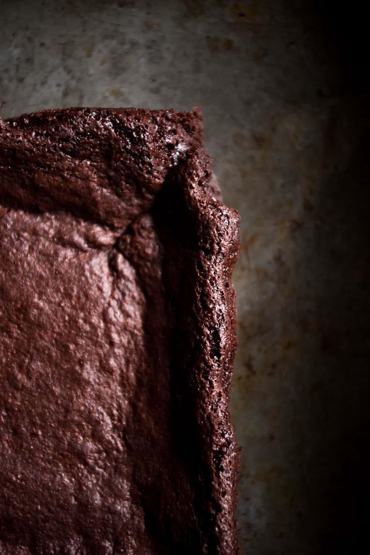 A macro image of the corner of a gluten free vegan brownie atop a dark steel backdrop