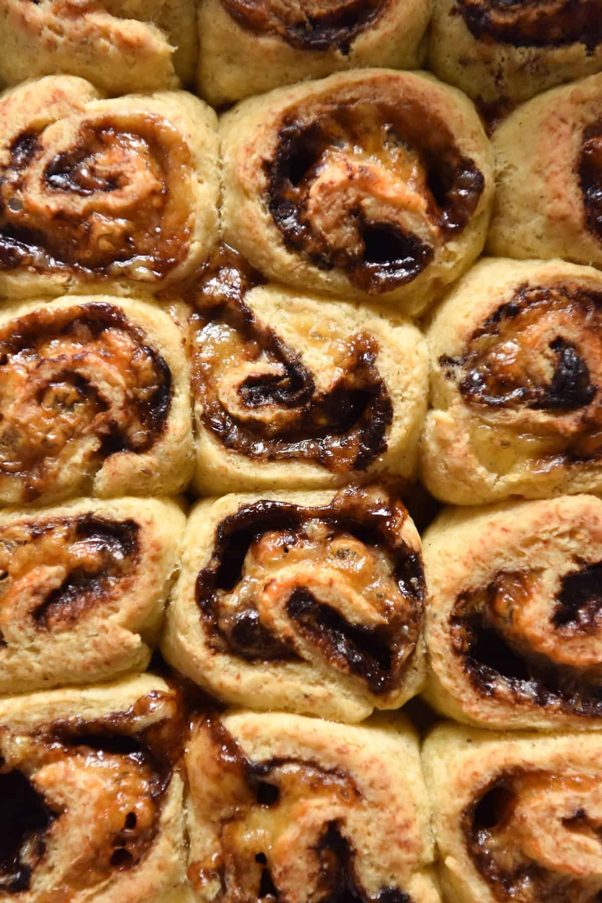 A close up macro image of gluten free Vegemite scrolls snug in a baking tray. The scrolls are golden brown and oozing with cheese and gluten free Vegemite. 