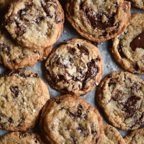 An aerial image of gluten free vegan choc chip cookies on a baking tray. The cookies are golden brown and studded with dark chocolate along with sea salt flakes.