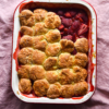 An aerial image of a gluten free strawberry cobbler in a white rectangular baking dish atop a pale pink linen backdrop.