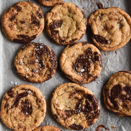 An aerial view of a baking tray lined with baking paper and topped with gluten free choc chip cookies.