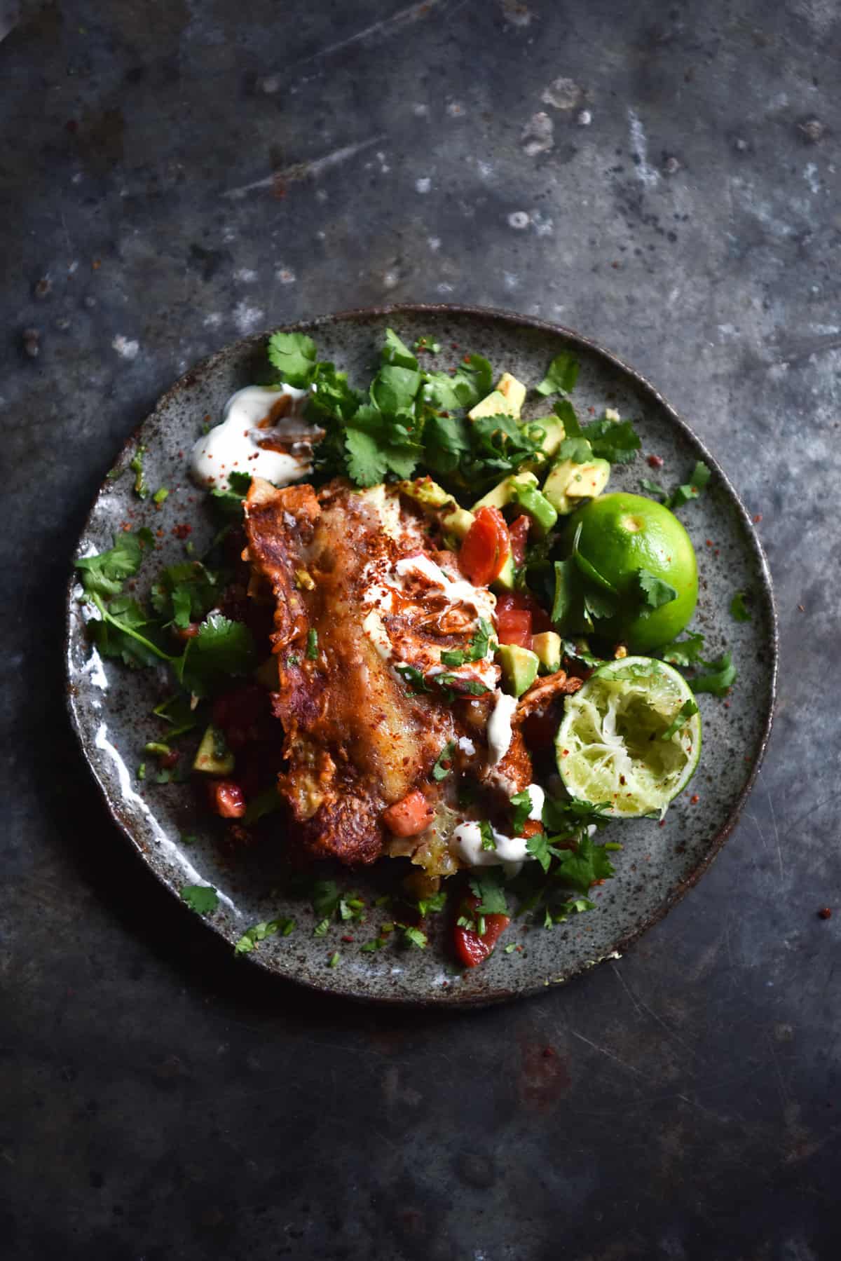 An aerial view of a plate of FODMAP friendly vegetarian enchiladas served with a herb salsa. The enchiladas sit on a dark blue ceramic plate against a dark blue steel backdrop