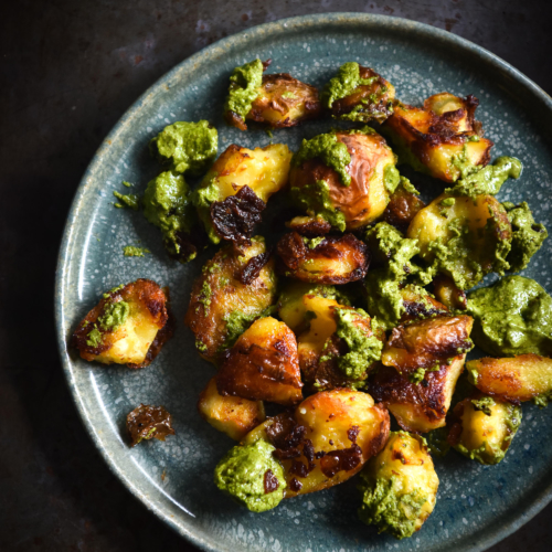 Crispy smashed potatoes with vegan rocket and almond pesto on a green ceramic plate against a dark steel backdrop