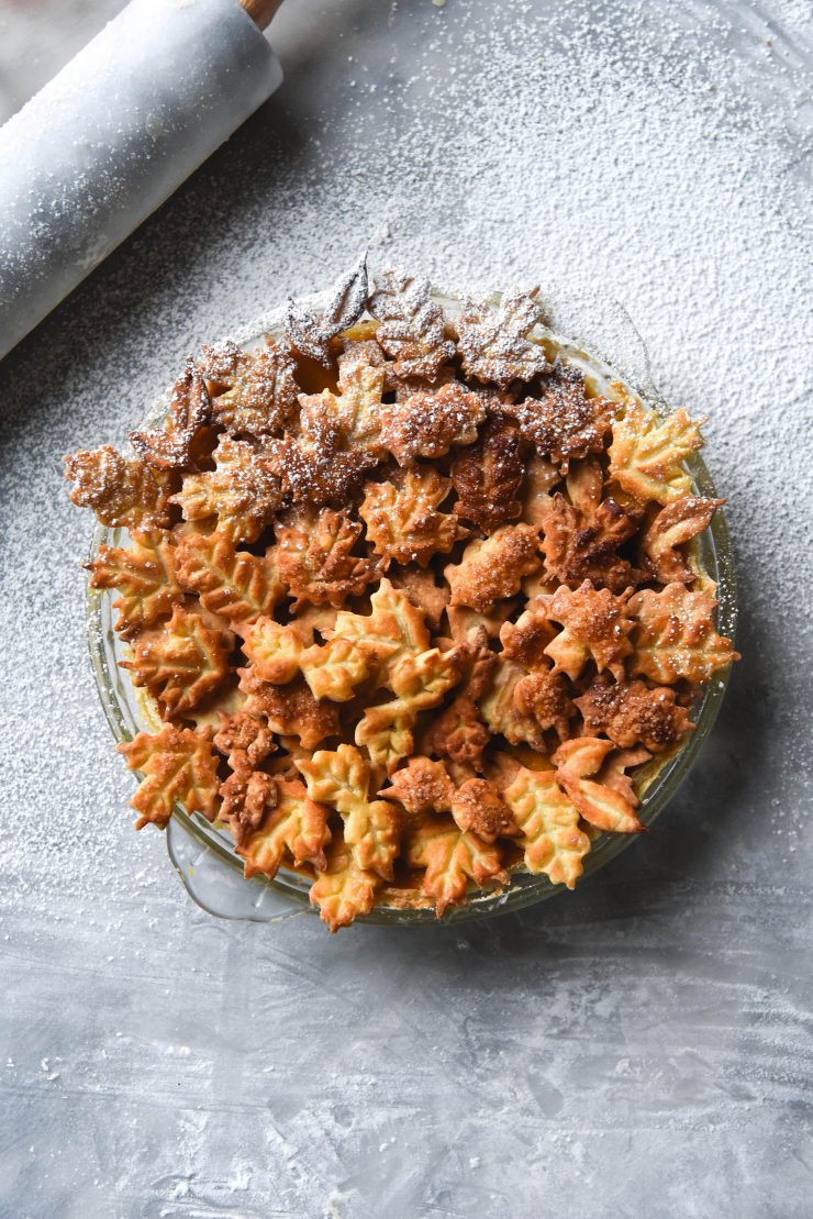 A gluten free pumpkin pie adorned with pastry leaves atop a white marble backdrop