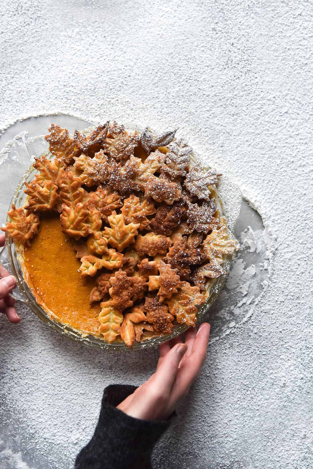 Gluten free pumpkin pie adorned with golden pastry leaves, sitting atop a backdrop of snow-like icing sugar