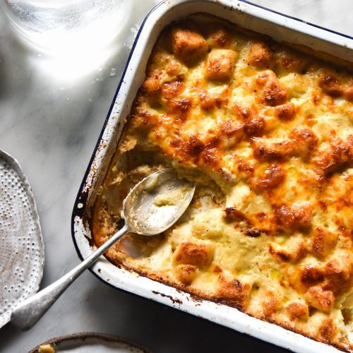 An aerial image of a bechamel gnocchi bake in a white baking dish atop a white marble table.