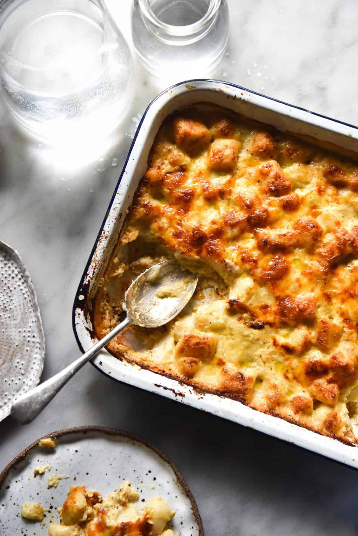 An aerial image of a bechamel gnocchi bake in a white baking dish atop a white marble table.