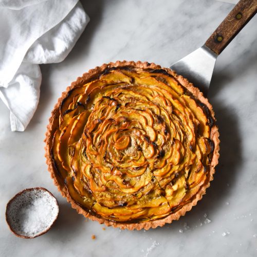 An aerial image of a gluten free savoury pumpkin tart on a white marble table