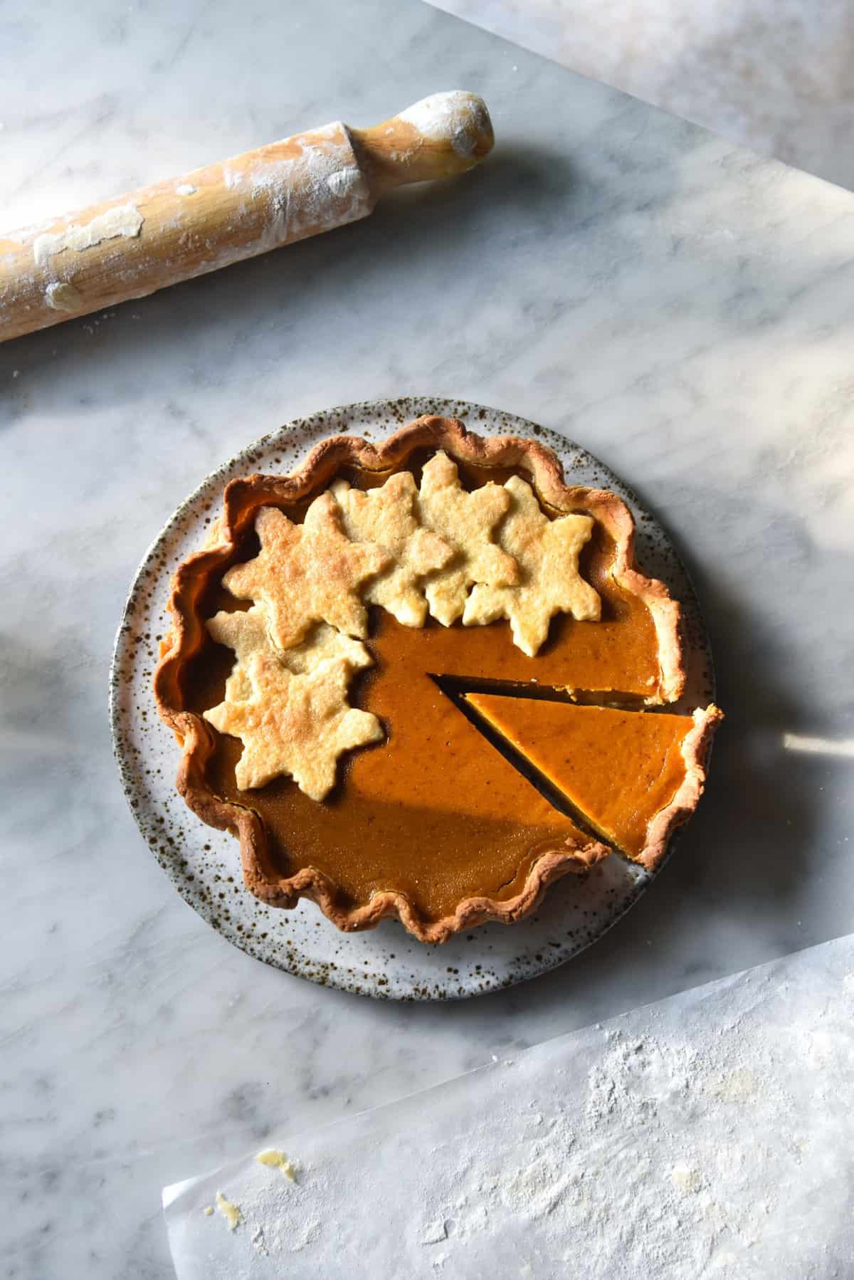 An aerial image of a gluten free pumpkin pie on a white marble table.