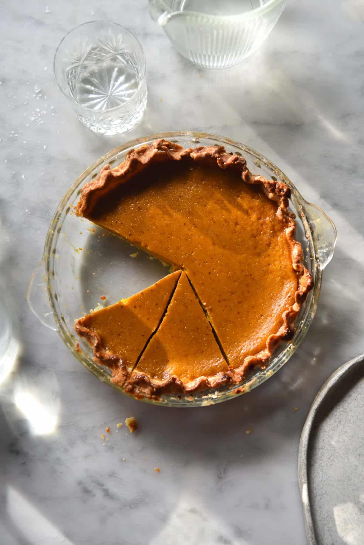 Low FODMAP pumpkin pie with flaky gluten free pastry and a refined sugar free filling on a white marble table in sunlight 