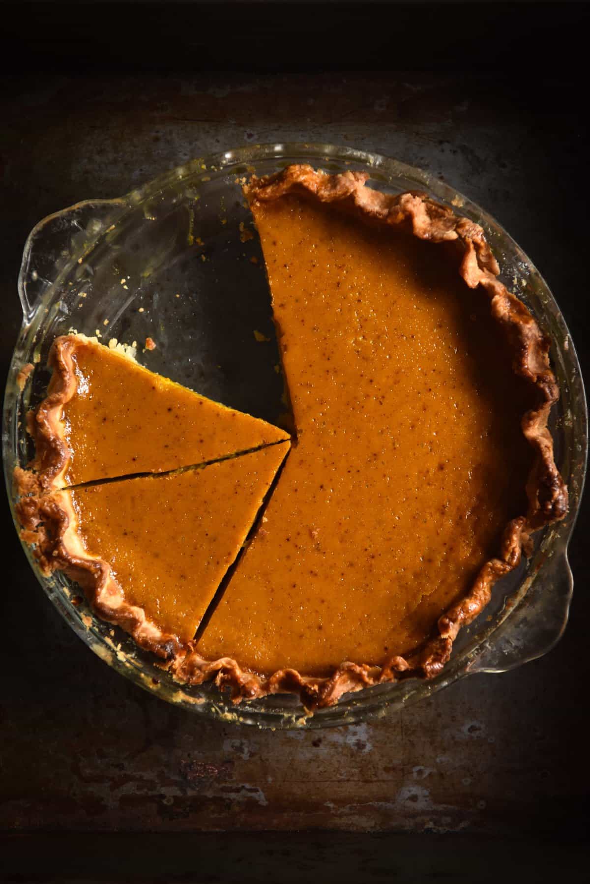 An aerial moody image of a gluten free pumpkin pie with one slice removed