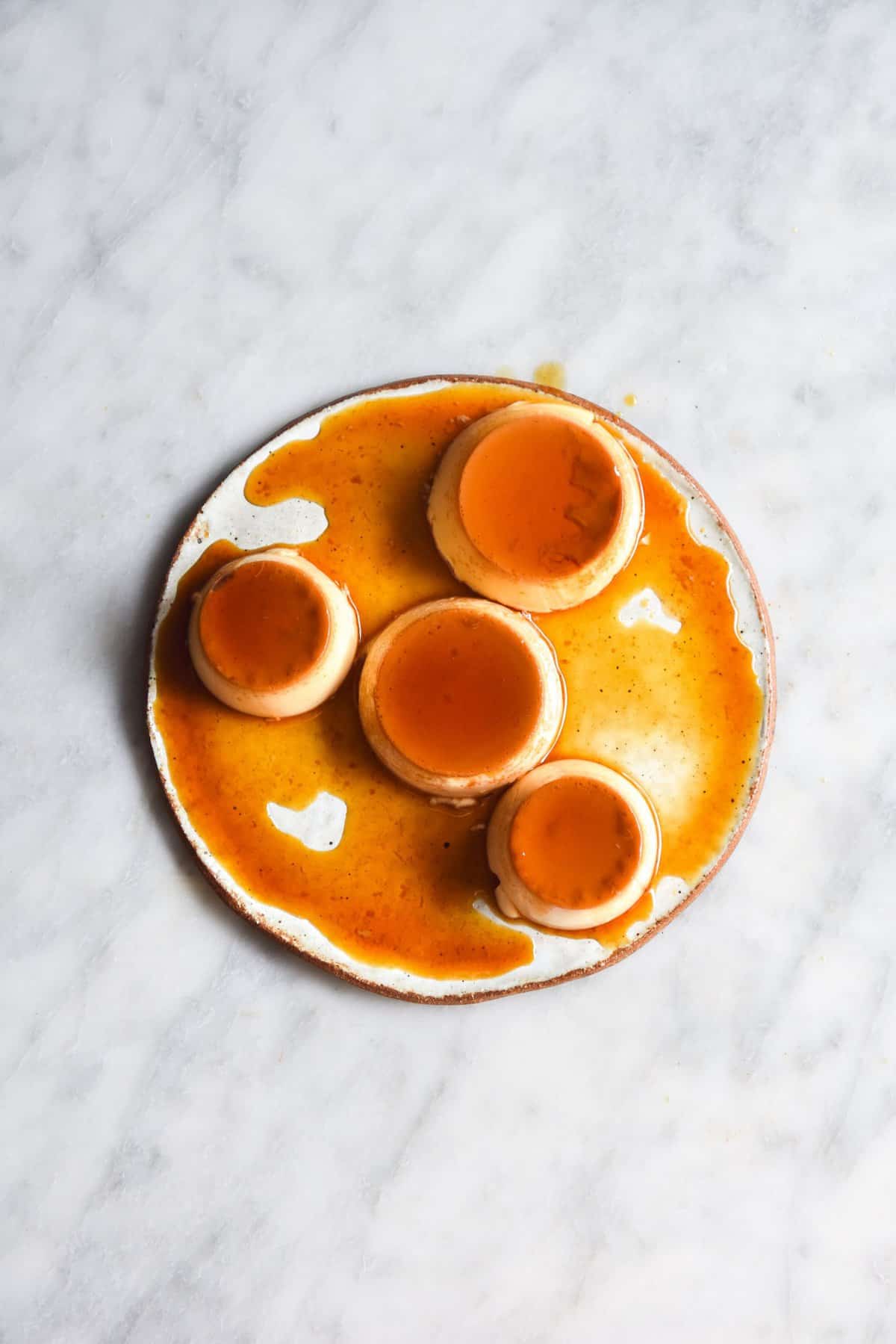 A white ceramic plate topped with 4 mini lactose free creme caramels on a white marble table