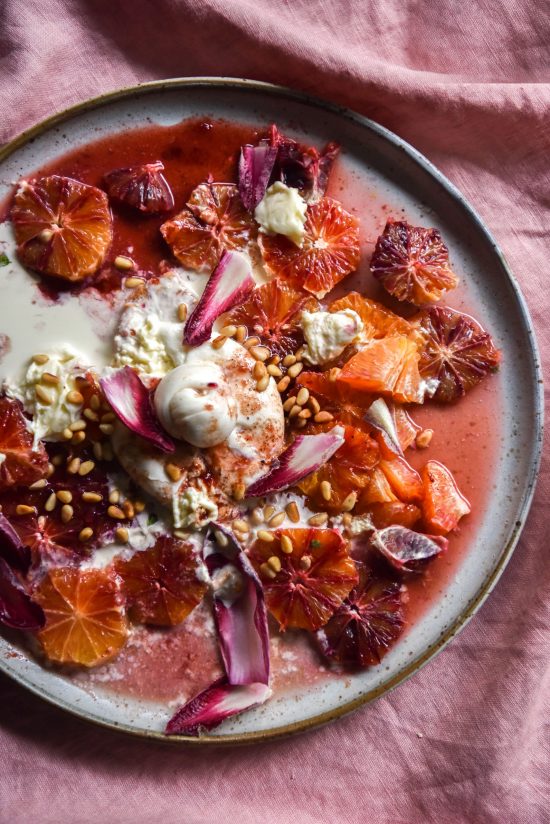 Blood orange, burrata, pine-nut salad with Christmas dressing sits atop a white ceramic plate on a pink linen backdrop