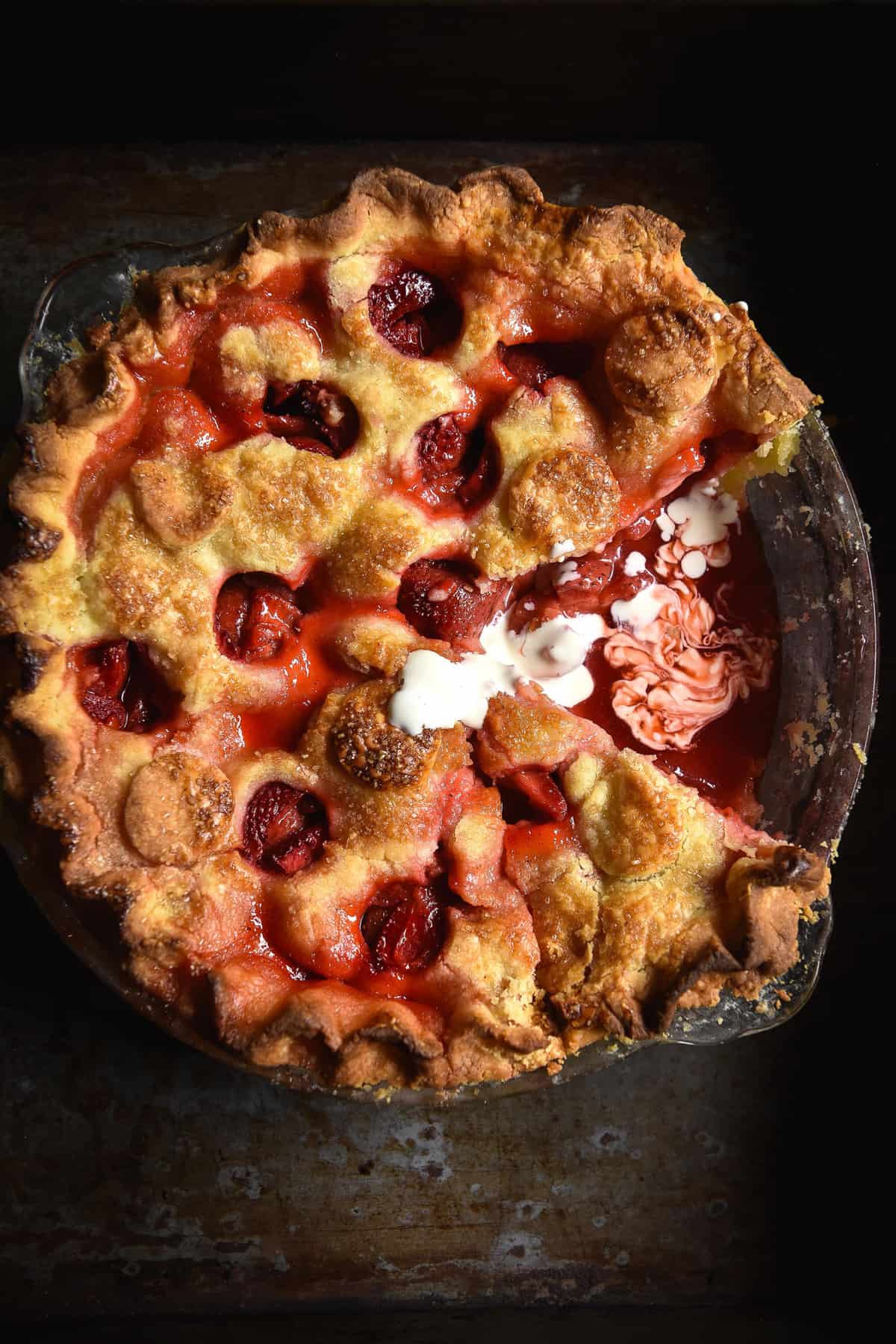 Gluten free strawberry pie on a dark steel backdrop. A piece of the pie has been removed and some cream has been drizzled on top.