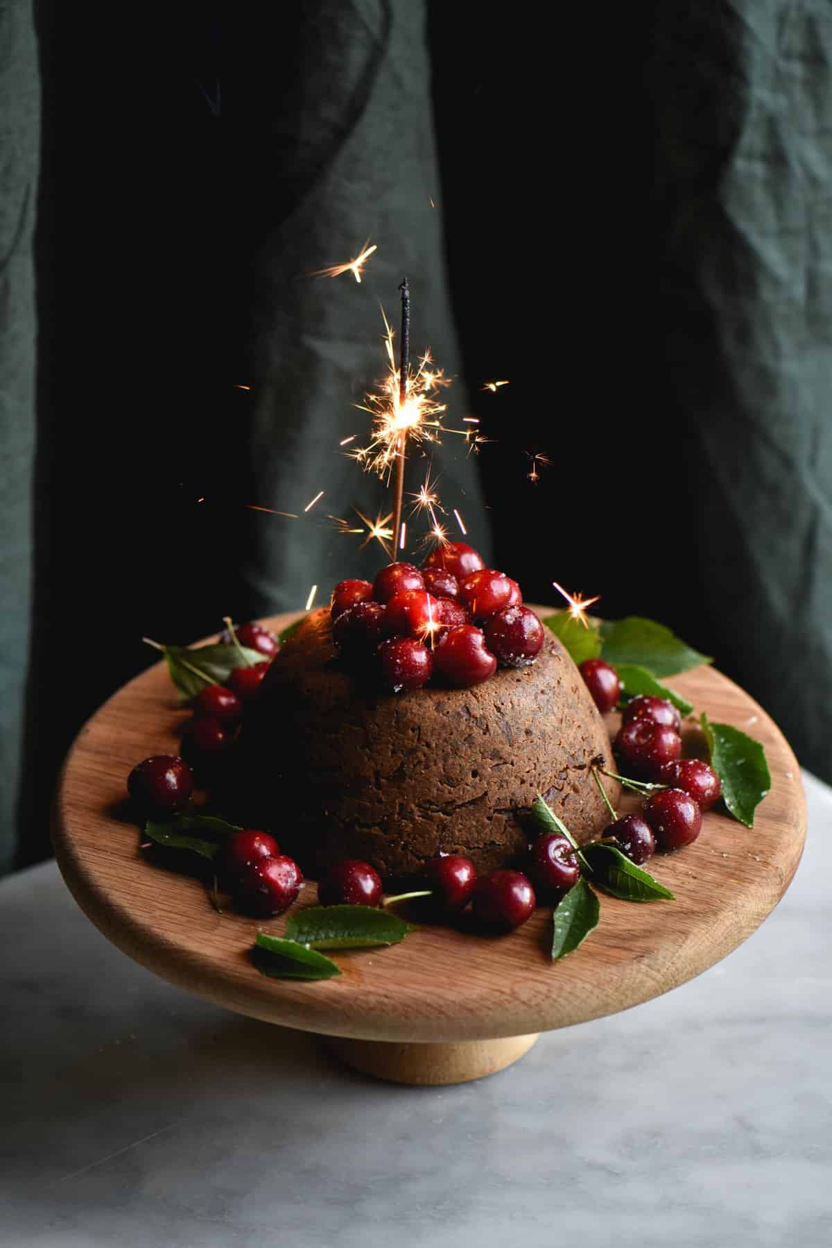 A fruitless, gluten free Christmas pudding topped with cherries and a sparkler
