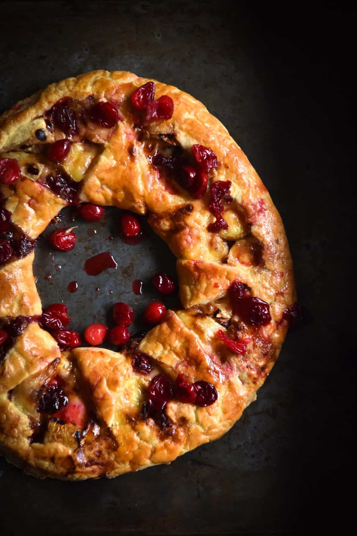 An aerial image of a gluten free brie and cranberry wreath on a dark steel backdrop.