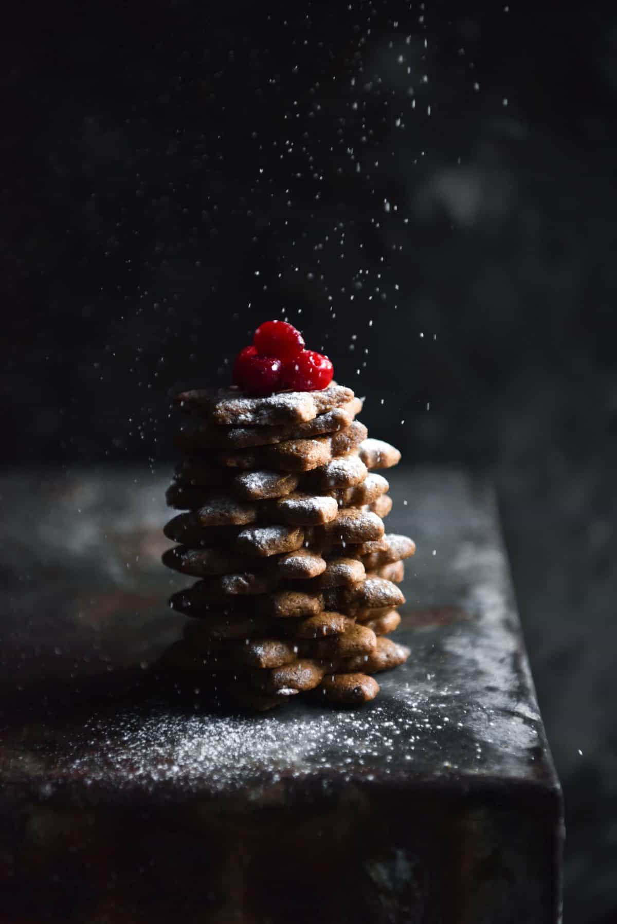 Gluten free gingerbread arranged to look like a mini Christmas tree against a dark and moody backdrop