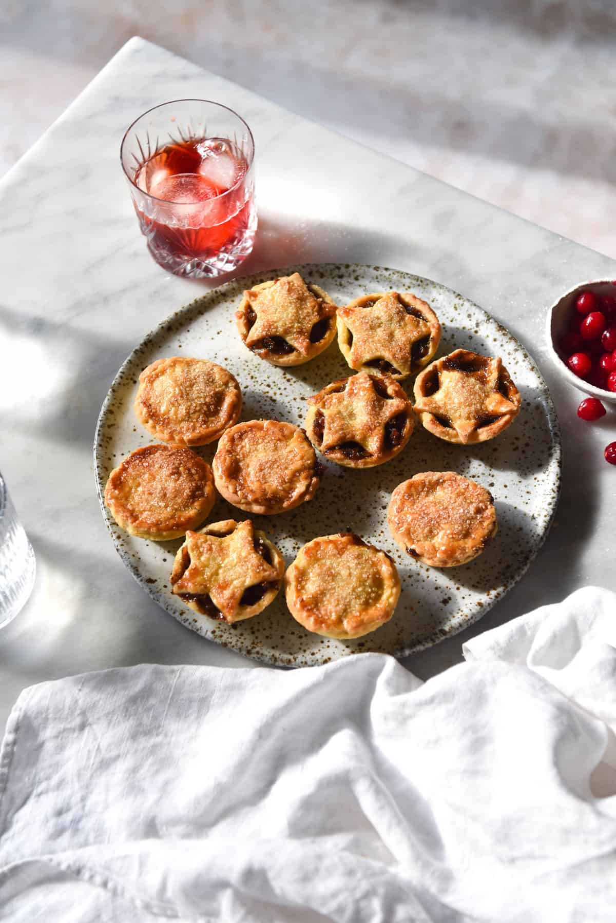 An aerial image of gluten free mince pies on a white speckled ceramic plate atop a white marble table.