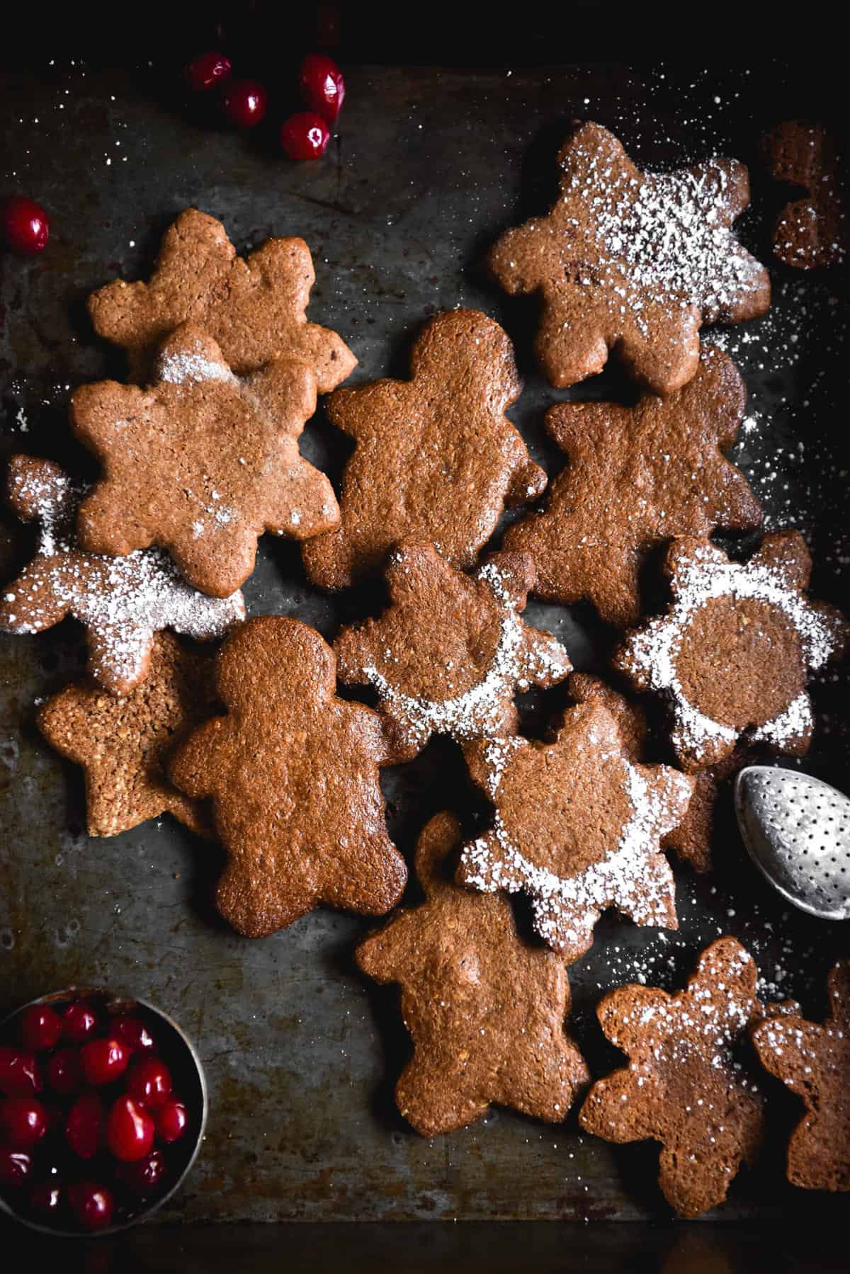 Grain free gingerbread arranged in a pile on a mottled dark blue steel backdrop. The gingerbread are cut into various shapes and some are sprinkled with icing sugar