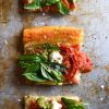 Squares of a gluten free tomato and pesto tart sit arranged in a line on a mottled sliver baking dish.