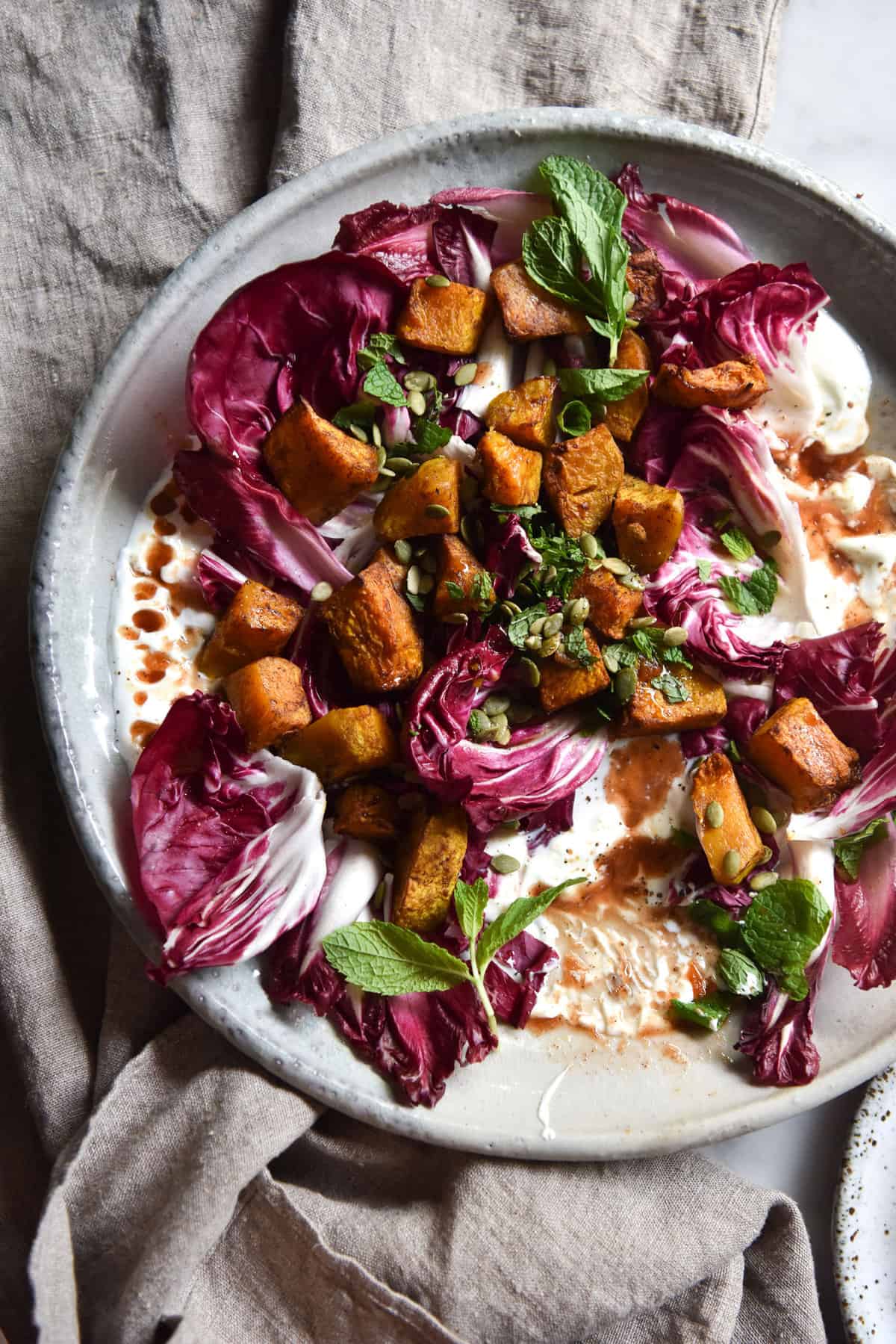 An aerial image of a spiced pumpkin salad on a bed of radicchio. The salad is on a white ceramic plate atop a beige linen tablecloth. 