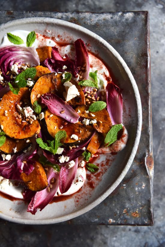 Spiced pumpkin salad with radicchio, mint, pine nut, feta and Christmas dressing on a white ceramic plate atop a dark blue steel backdrop