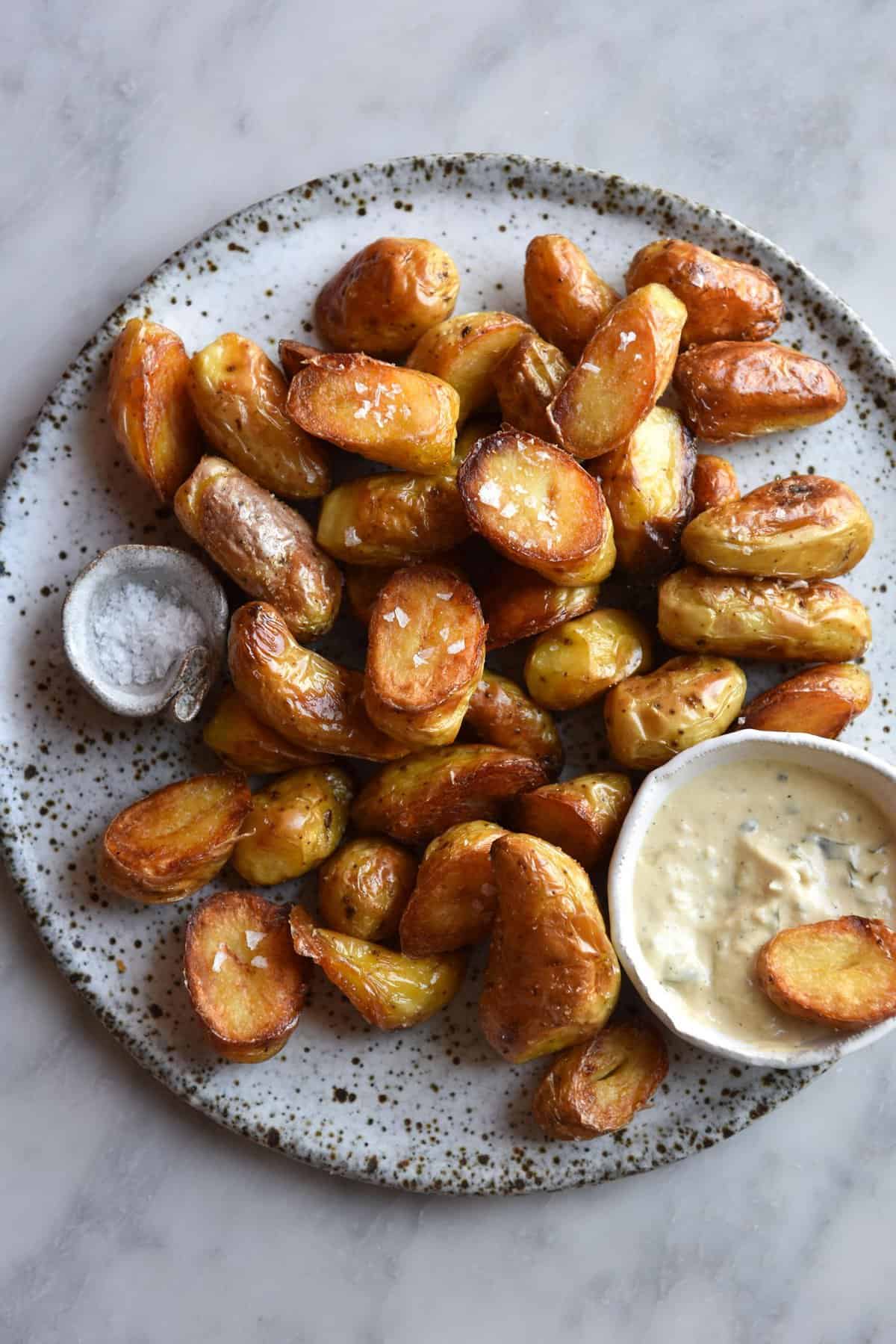 Vegan Caesar salad dressing in a white ceramic bowl on a plate topped with crispy roast potatoes. The plate sits atop a white marble table.