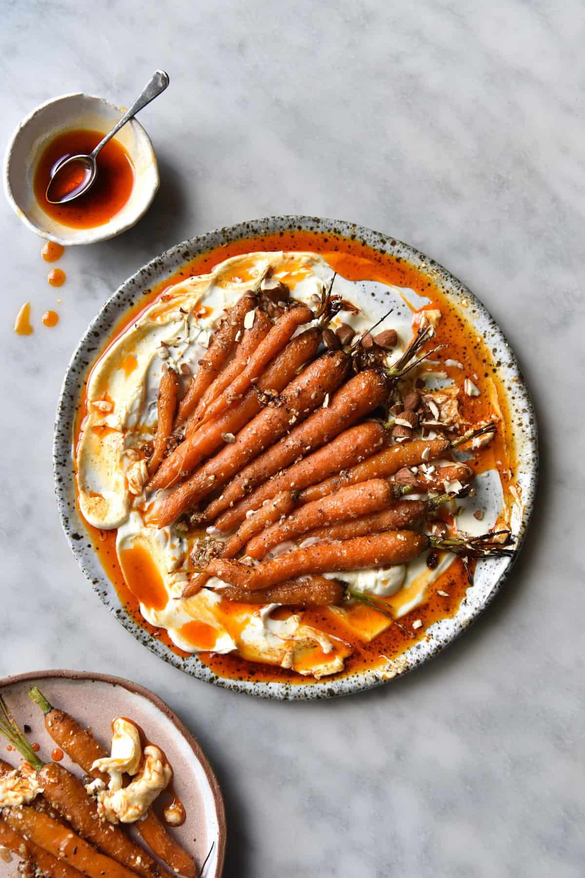 Dukkah roasted carrots with labne and aleppo chilli oil on a white ceramic plate atop a white marble table