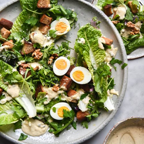 Vegetarian, Gluten Free and FODMAP Friendly Caesar Salad on a white plate atop a white marble table.