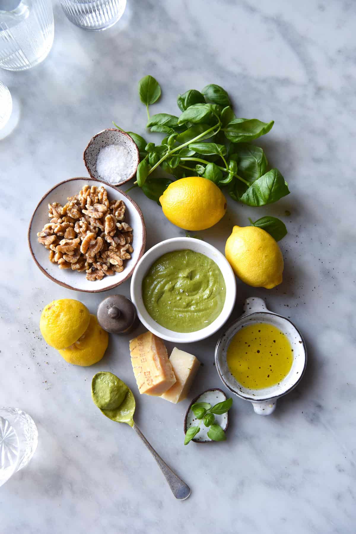 An aerial image of the ingredients used for a FODMAP friendly pesto arranged in a group on a white marble table