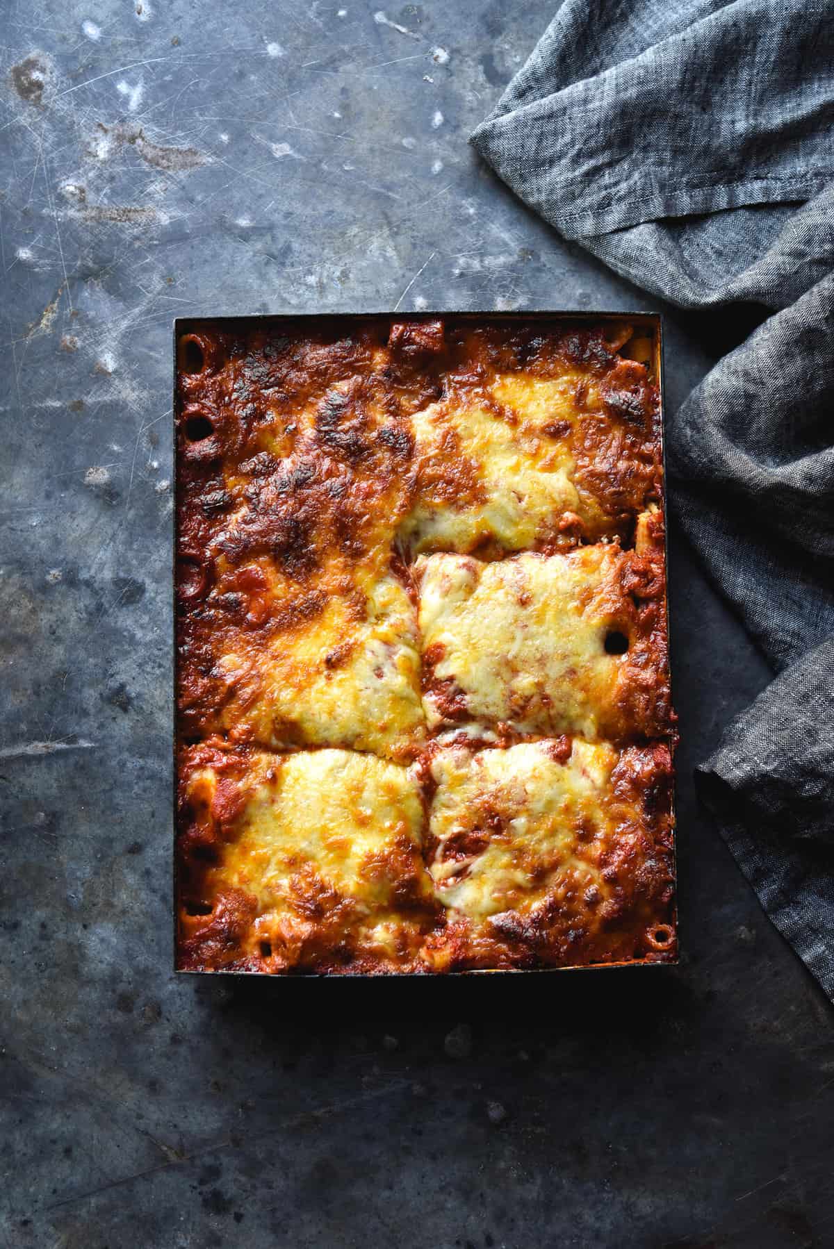 An aerial image of a cheesy gluten free pasta bake on a dark blue steel backdrop