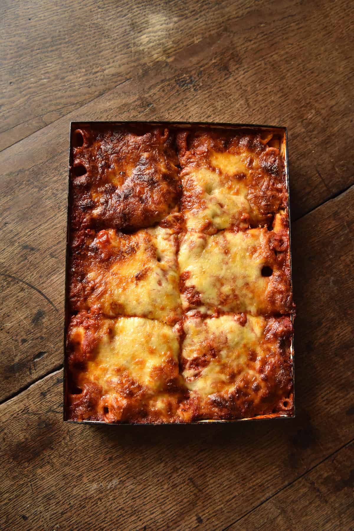 An aerial view of a spinach and ricotta pasta bake sitting atop a wooden table. The bake is cheesy and golden which compliments the warm tones of the wood.