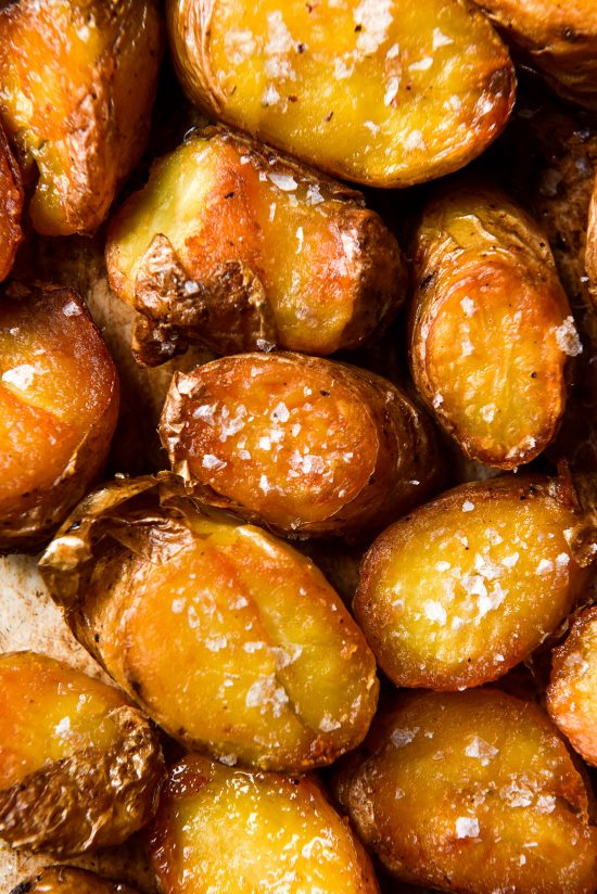 An aerial close up image of a tray of golden brown crispy roasted potatoes topped with flaky sea salt