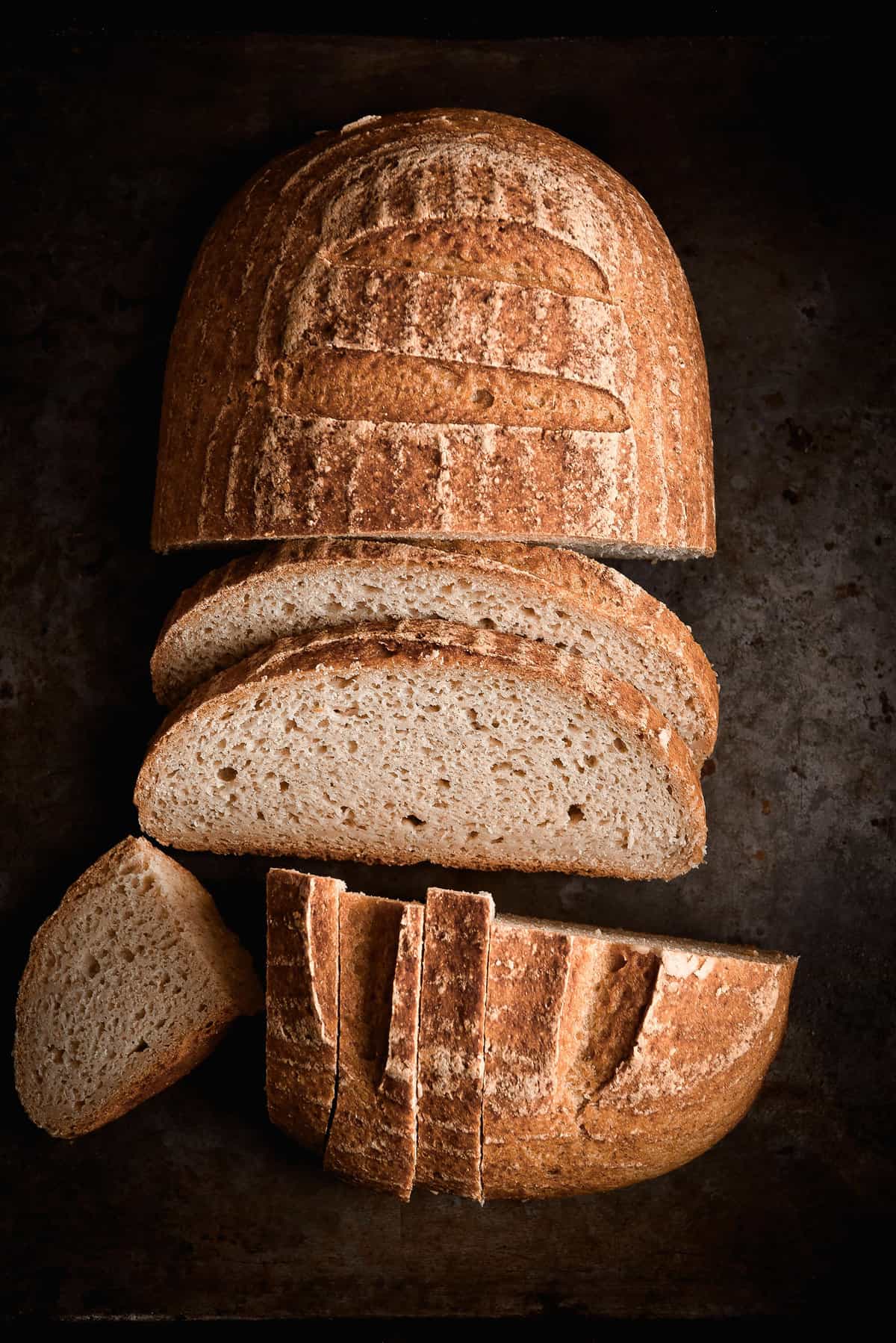 A moody aerial photo of a loaf of gluten free sourdough bread that has been sliced.