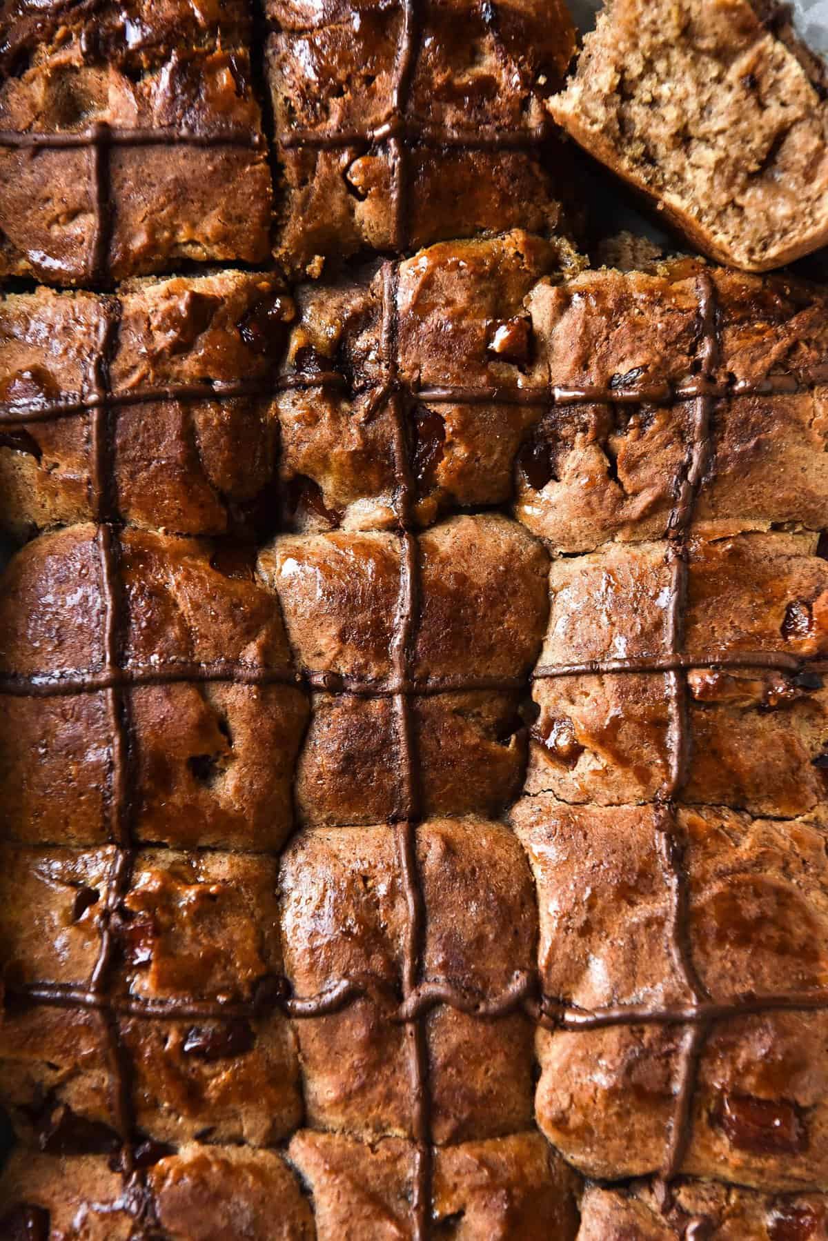 An aerial close up of a tray of golden brown gluten free sourdough hot cross buns topped with chocolate crosses. 