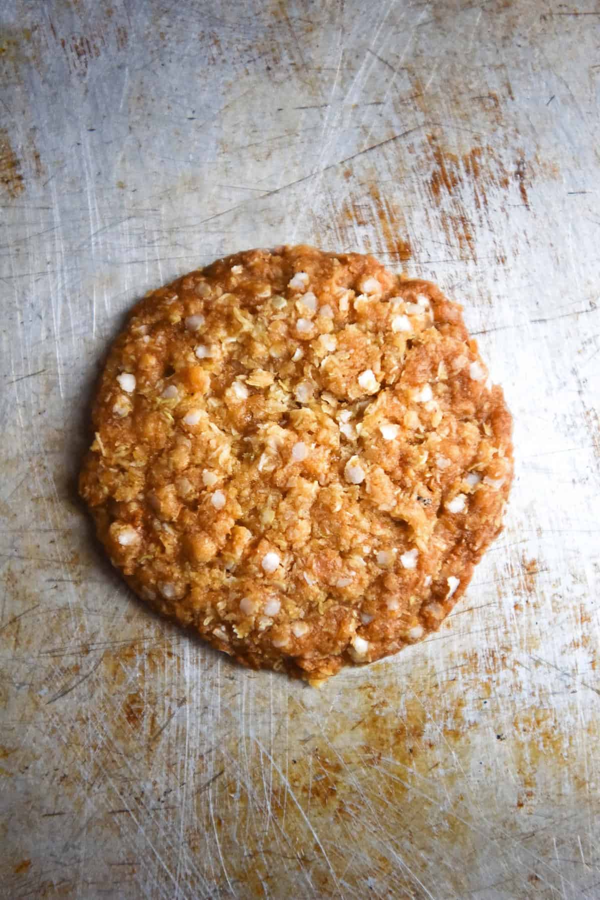 An aerial image of a gluten free ANZAC biscuit atop a steel baking tray.