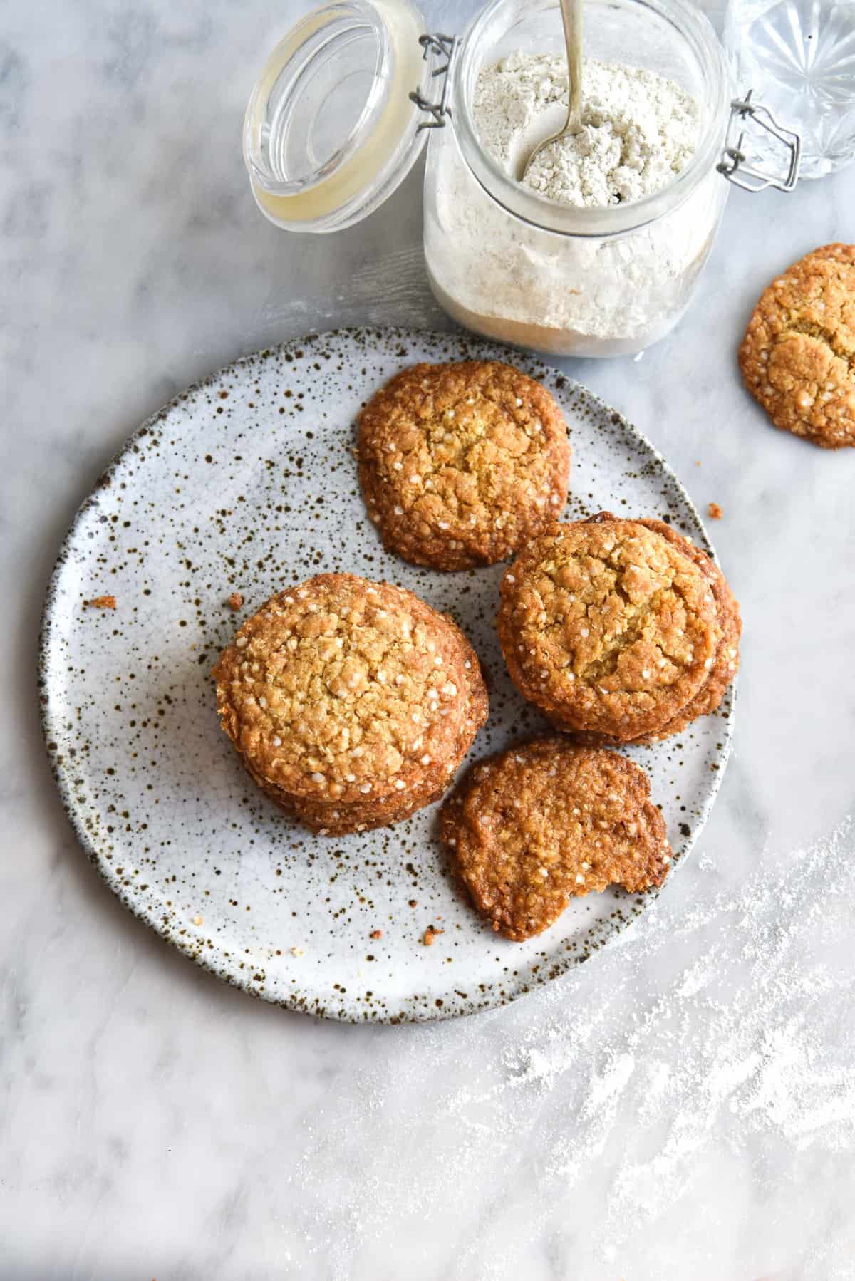 An aerial image of a stack of gluten free ANZAC cookies on a white speckled ceramic plate atop a white marble table. 