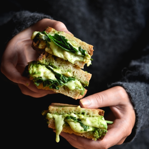 A moody side on image of pesto and cheese toasties being held by a person wearing a dark grey fluffy jumper.