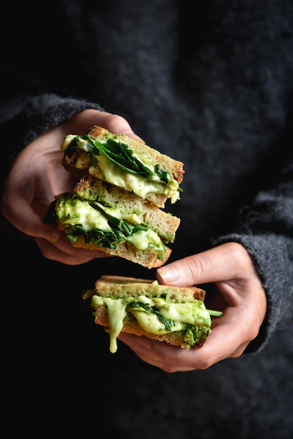 A moody side on image of pesto and cheese toasties being held by a person wearing a dark grey fluffy jumper.
