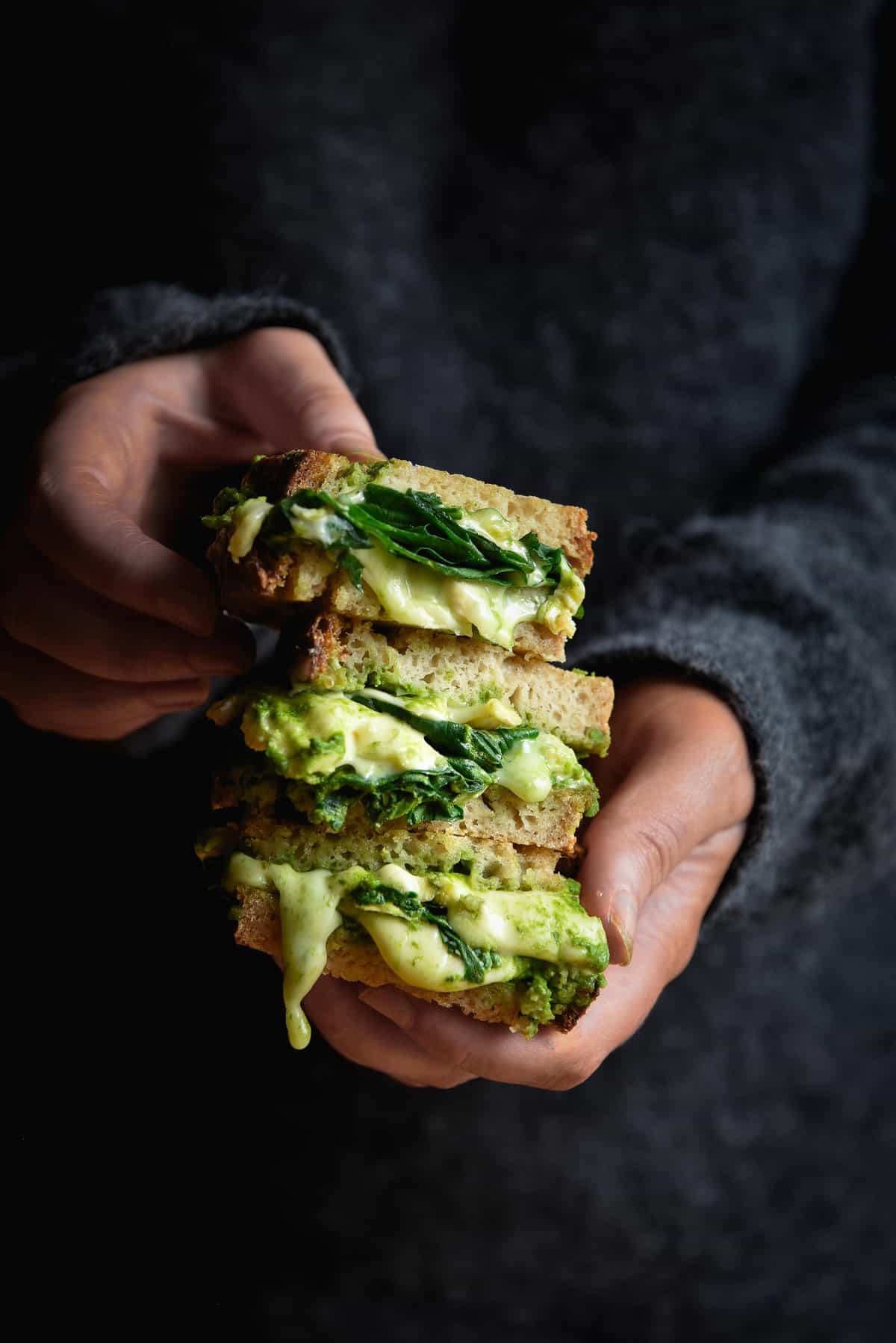 A stack of gluten free green toasties filled with D'Affinois cheese held by a person in a dark grey fluffy jumper. The image is part of a series on Vegetarian cheese in Australia.