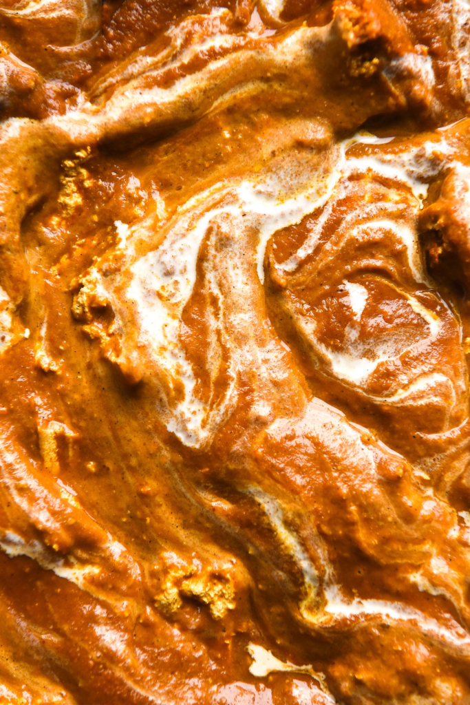 A macro close up photo of the top of a FODMAP friendly paneer curry. The curry is a deep orange and has been swirled with cream, creating a marbled effect