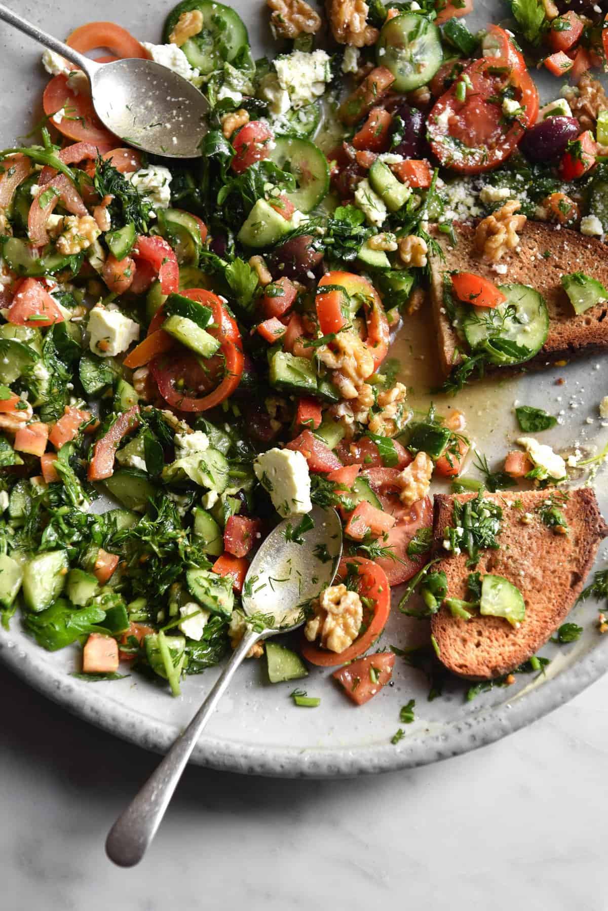 A close up aerial image of a FODMAP-friendly tomato and cucumber salad on a white ceramic plate