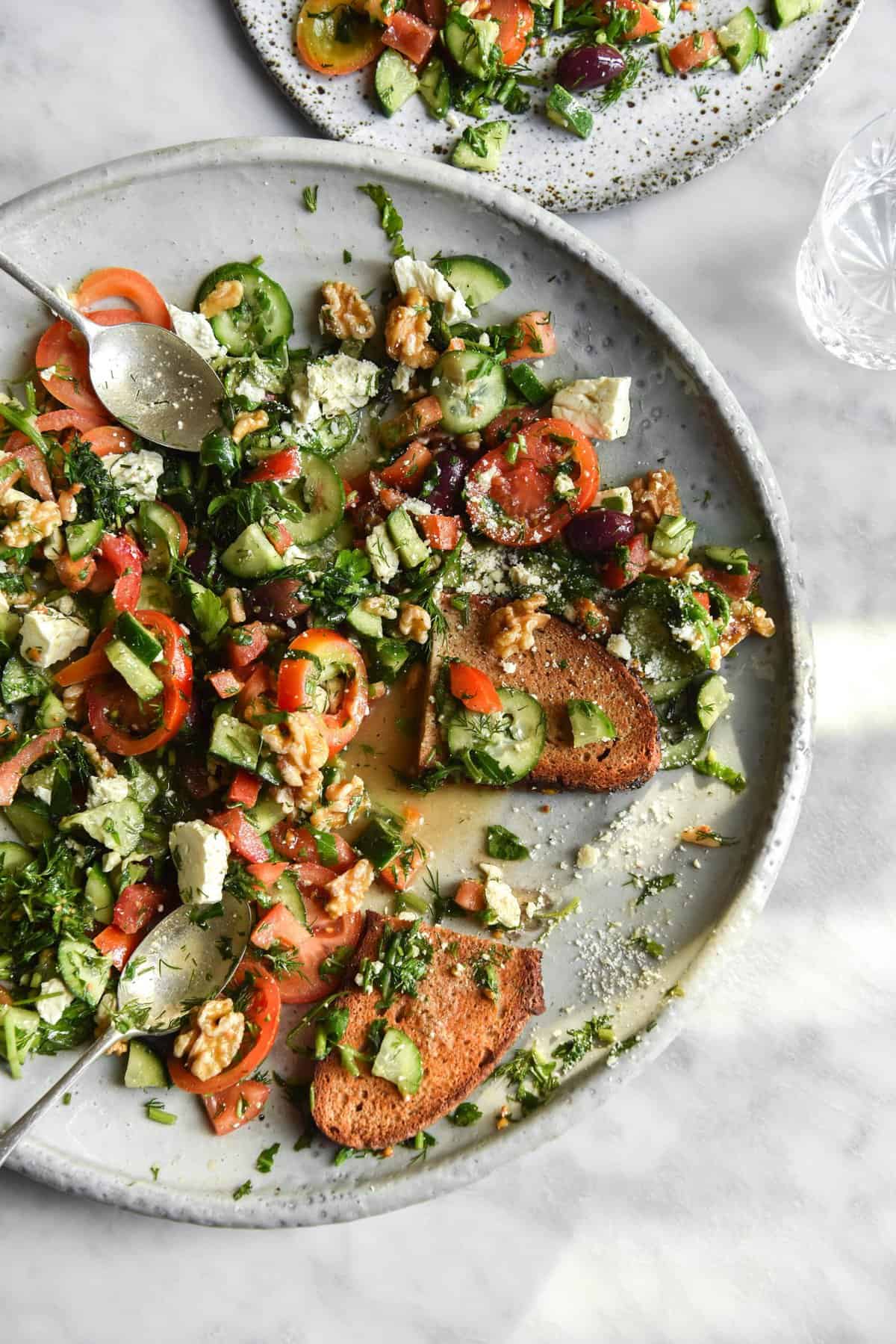 FODMAP-friendly tomato and cucumber salad on a large white ceramic plate atop a brightly lit white marble table. 