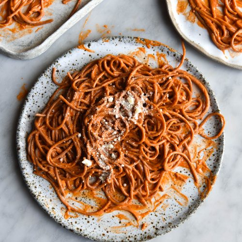 Three white ceramic plates of FODMAP friendly Pasta Alla Vodka on a white marble table. The pasta is topped with extra finely grated Parmesan cheese.