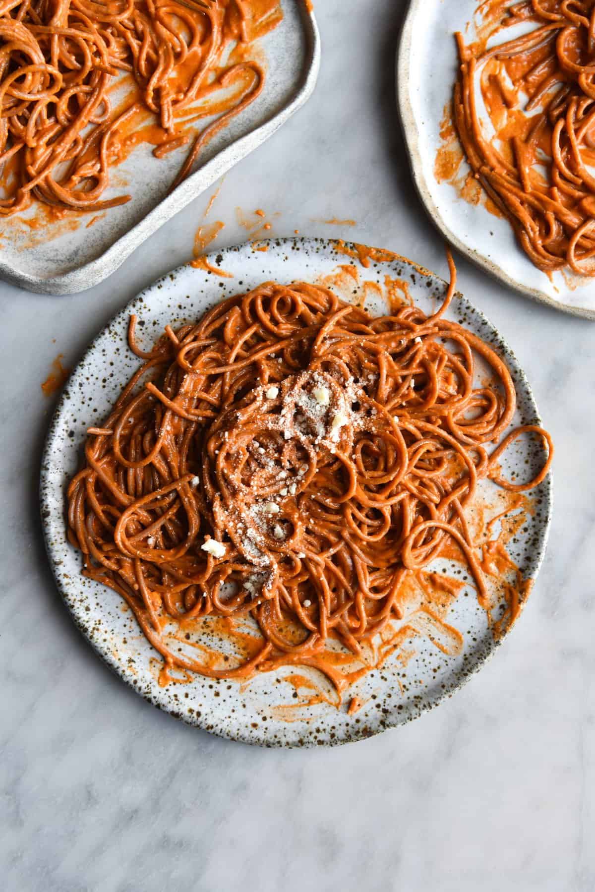 Three white ceramic plates of FODMAP friendly Pasta Alla Vodka on a white marble table. The pasta is topped with extra finely grated Parmesan cheese.