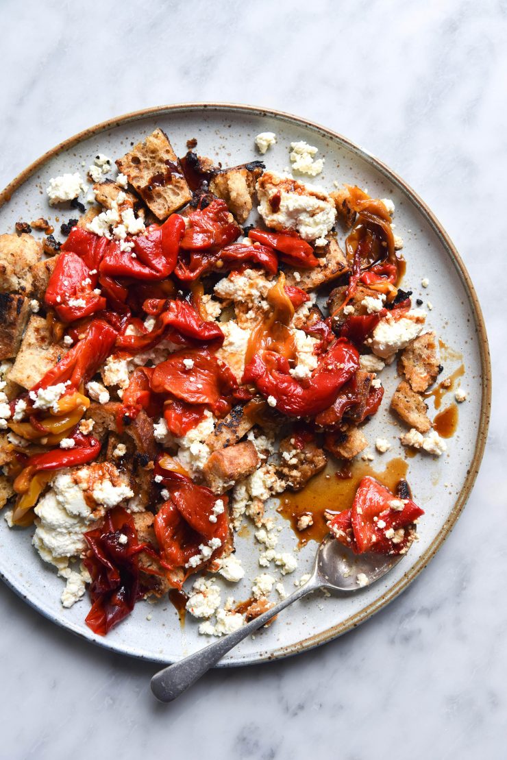 An aerial image of a plate of gluten free sourdough croutons with homemade lactose free ricotta, roasted capsicums and a balsamic glaze. The plate sits atop a white marble table.