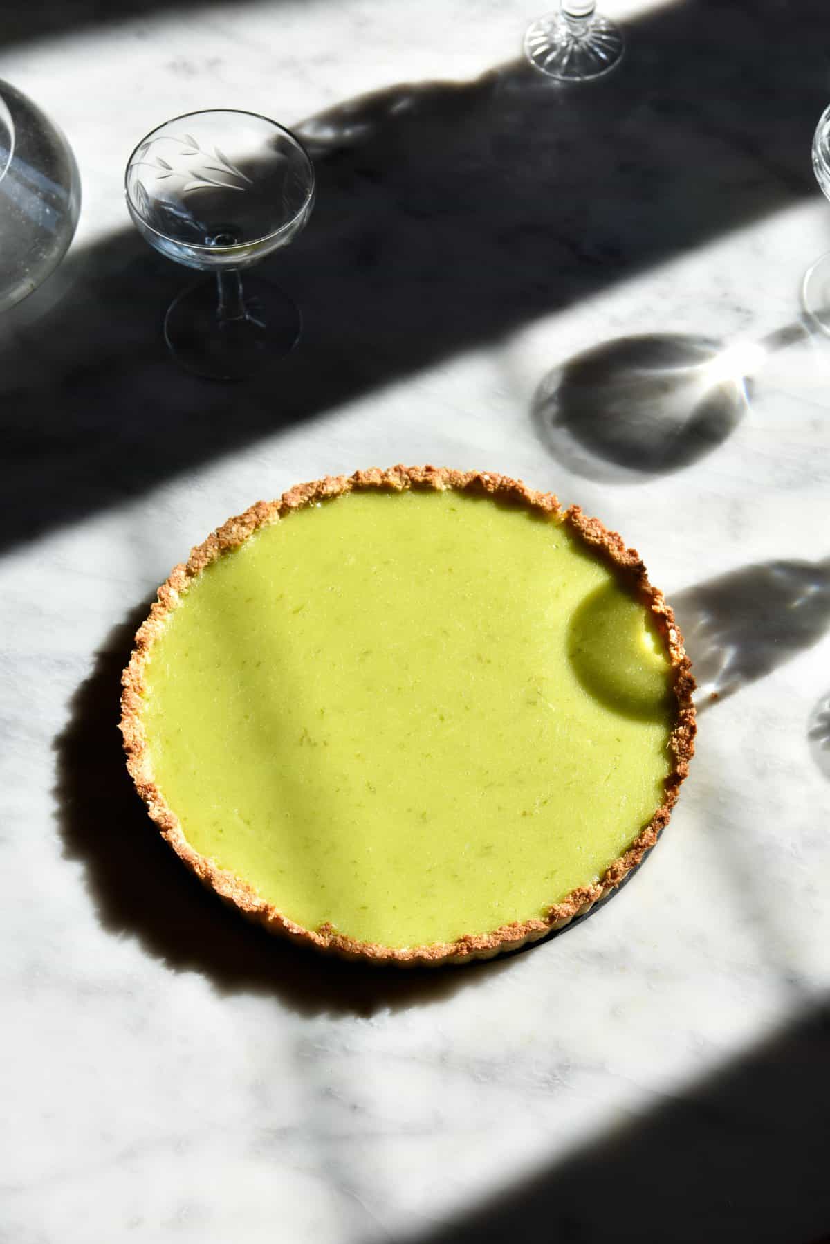 An aerial sunlit image of a gluten free lime curd tart on a white marble table.