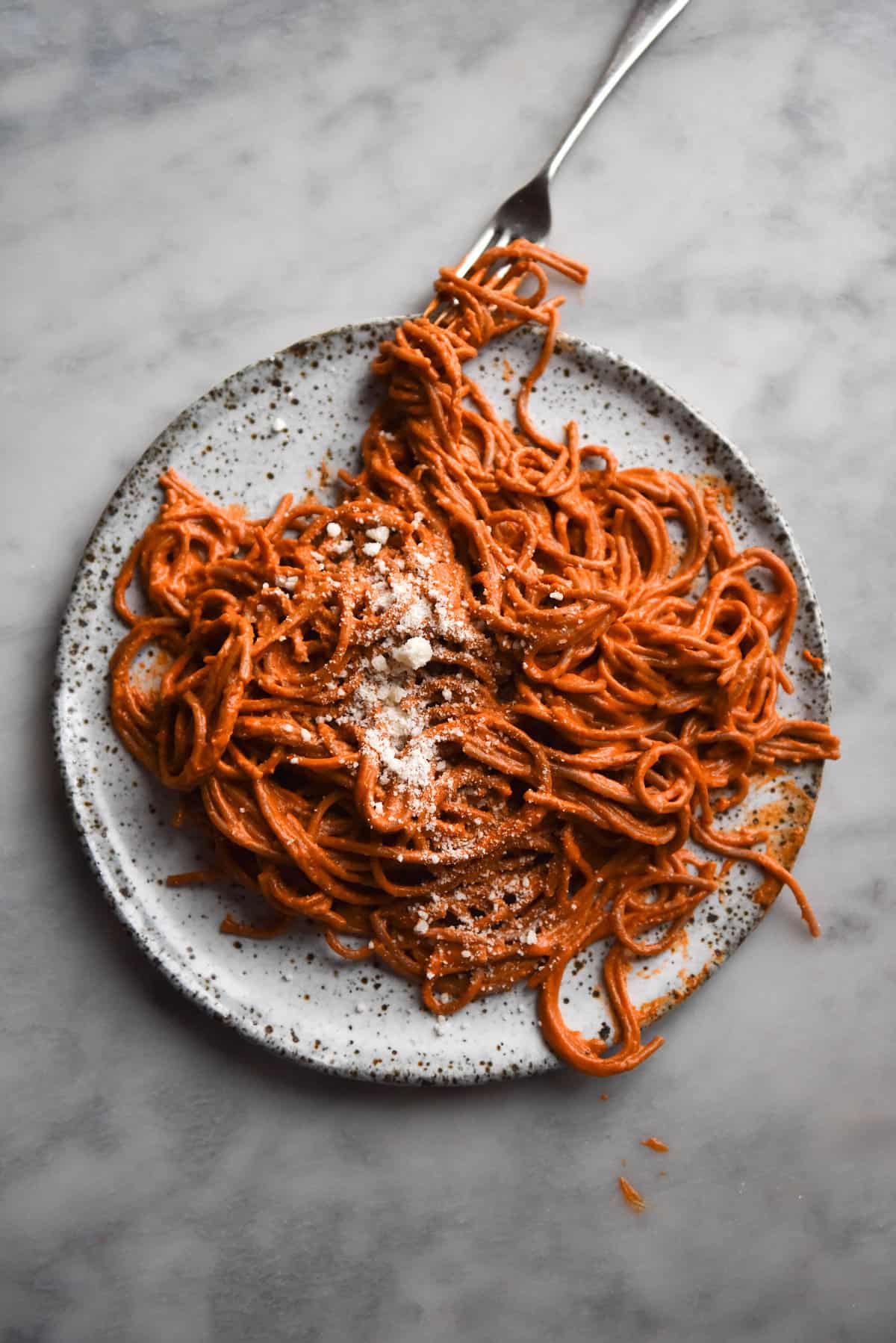 An aerial image of a white speckled ceramic plate topped with pasta alla vodka. The pasta is casually swirled on the plate which sits atop a white marble table. 