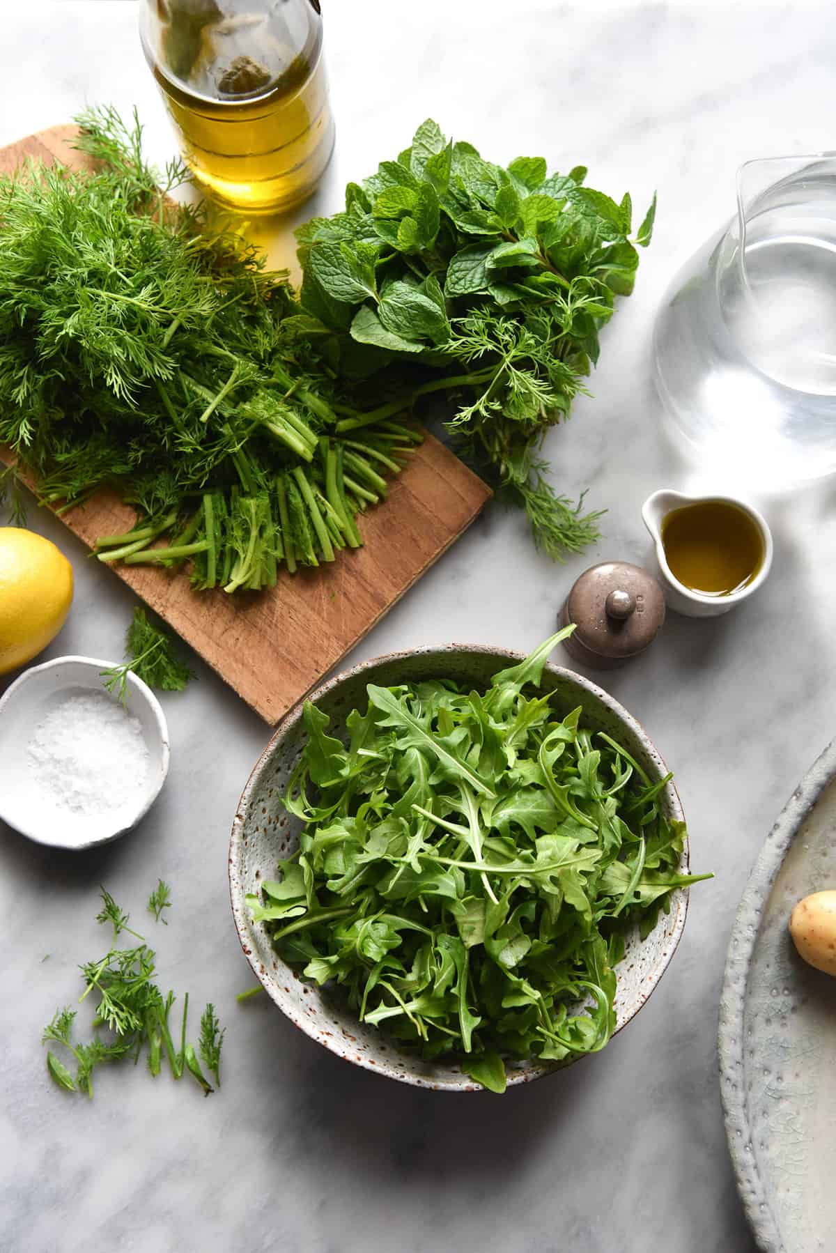 An aerial image of the ingredients used in a low FODMAP potato salad arranged on a white marble table.