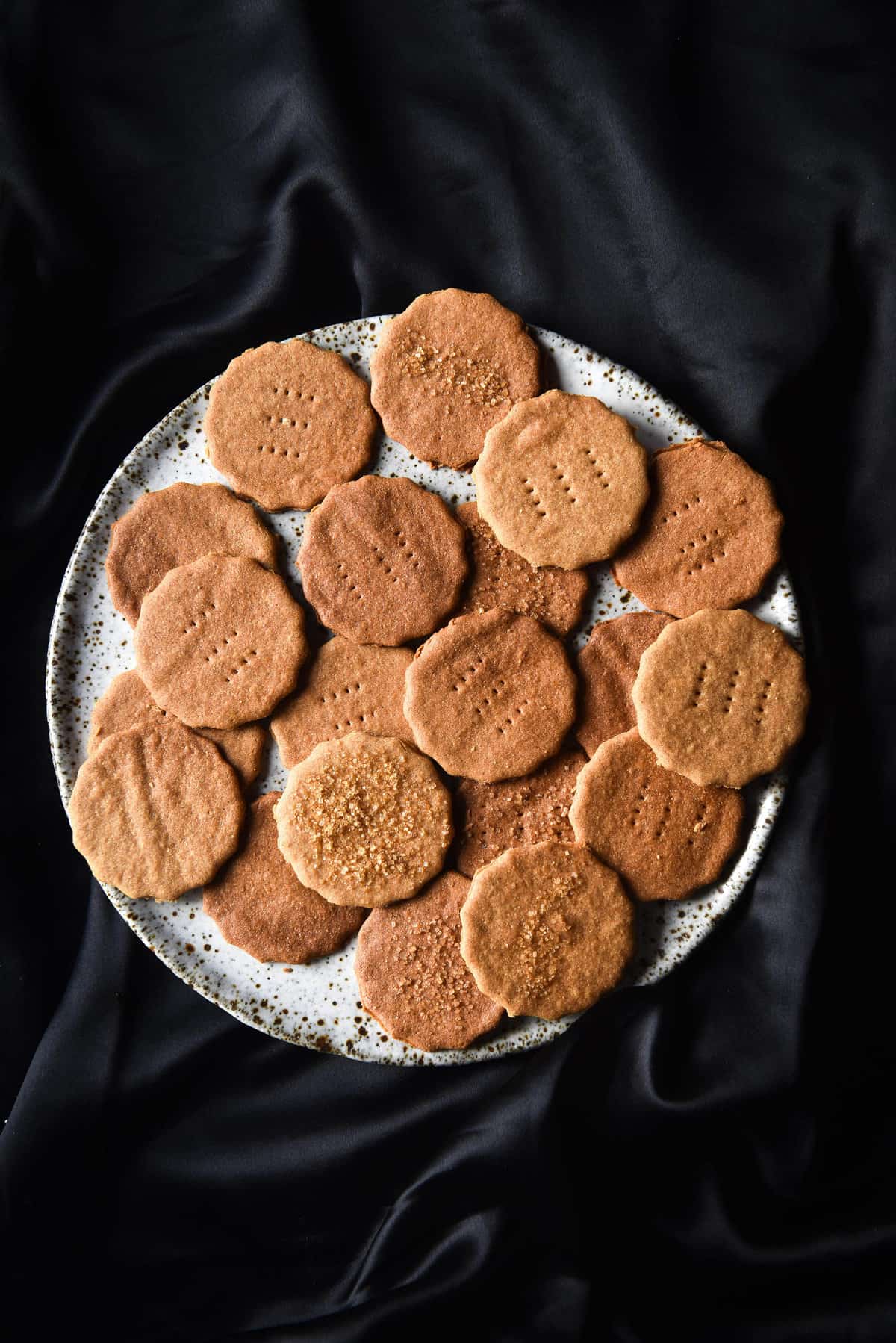 An aerial view of a plate of gluten free Graham crackers on a white ceramic plate that sits on a silky black fabric